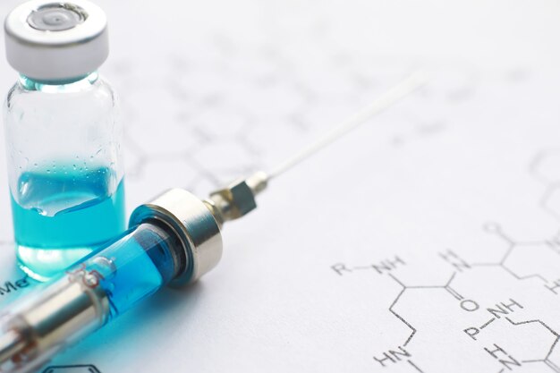 Frascos pequenos com injeção e seringa para injeção em fundo azul perto da fórmula química