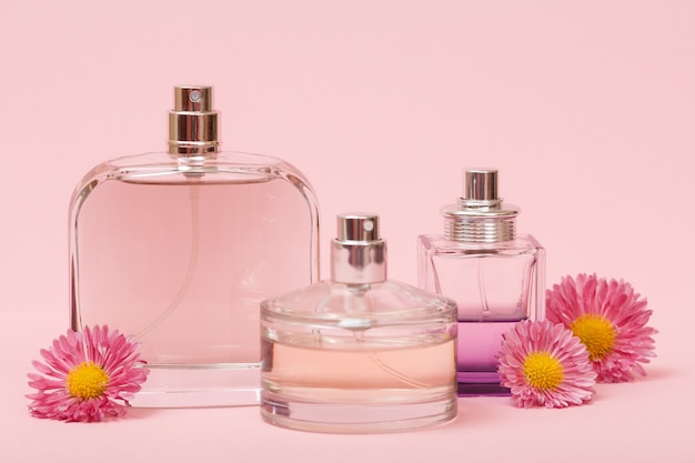 Frascos con perfume de mujer y capullos de flores sobre un fondo rosa. Productos de mujer.