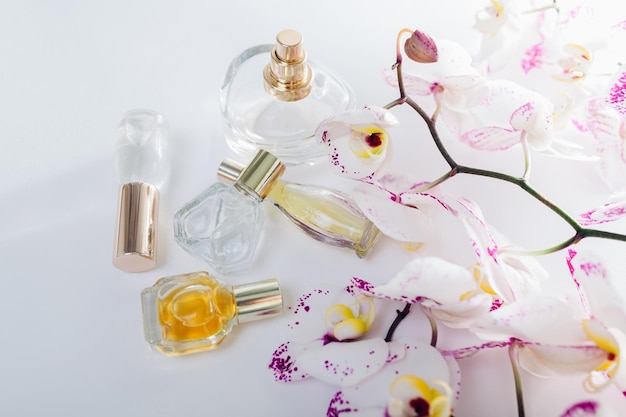 Frascos de perfume con orquídea blanca con manchas moradas sobre fondo blanco.