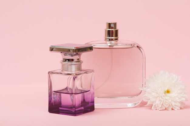 Frascos con perfumes femeninos y capullo de flor en un fondo rosa. Productos de mujer.