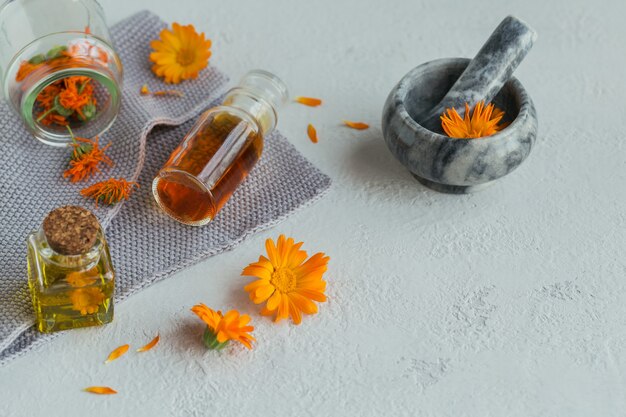 Frascos de tintura o infusión de caléndula y aceite esencial con flores de caléndula frescas y secas a la luz