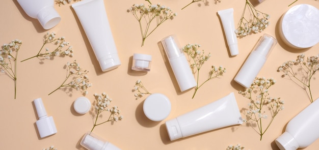 Frascos de tubos de plástico blanco y ramas de gypsophila en contenedores de fondo beige para publicidad de cremas y geles cosméticos y promoción de marca vista superior