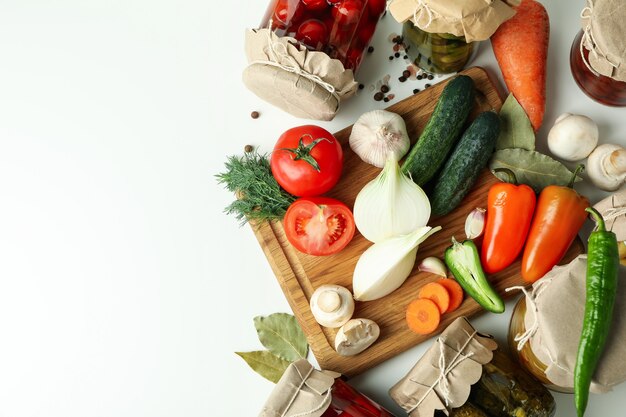 Frascos de verduras en escabeche e ingredientes en mesa blanca