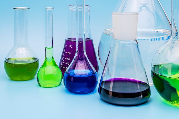 Frascos de vidrio de laboratorio médico de diferentes tamaños con líquidos de diferentes colores sobre un fondo azul. Tubos y equipos de laboratorio. El concepto de experimentos de laboratorio.
