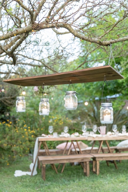 Frascos de vidrio con velas dentro de una decoración rústica colgando de una madera en un jardín.