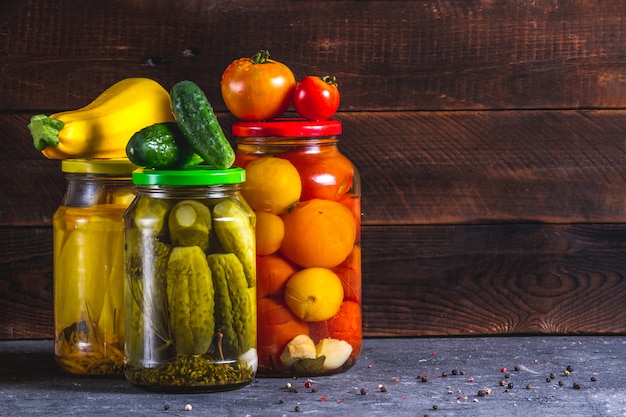 Frascos de vidrio en vinagre, pepinos frescos, calabacines y tomates sobre un fondo de madera. Copia espacio