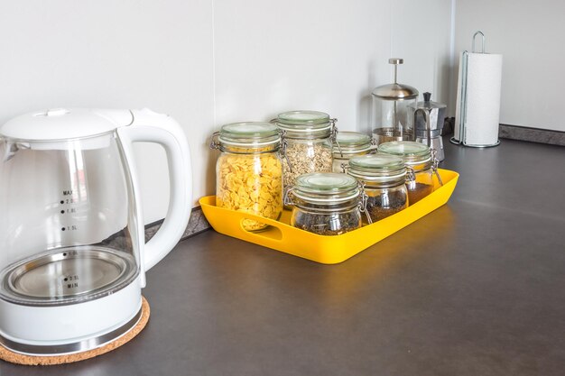 Frascos vintage con estilo de vidrio con diferentes alimentos y tetera en el interior de la cocina moderna en un apartamento tipo loft de estilo minimalista con copos de maíz de avena de color amarillo, té de café