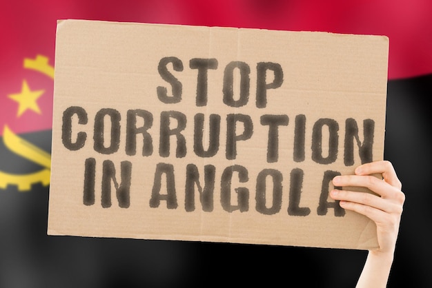 La frase Alto a la Corrupción en Angola en una pancarta en la mano de los hombres con una bandera angoleña borrosa en el fondo Prohibido Prevenir el delito de riqueza Corrupción Economía Corruptible Político