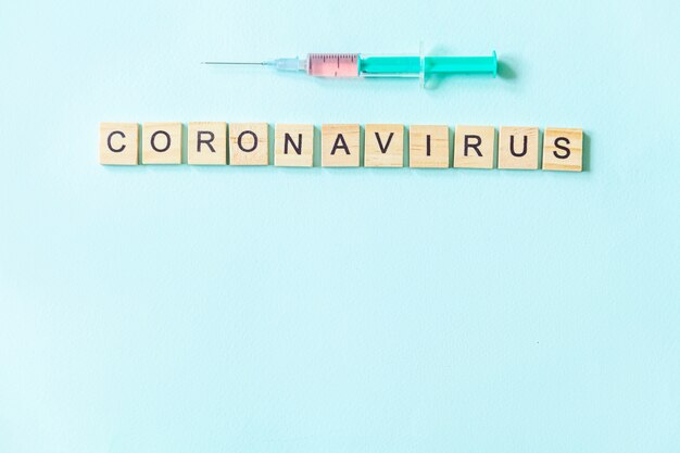 Frase de texto Coronavirus e seringa sobre fundo azul pastel