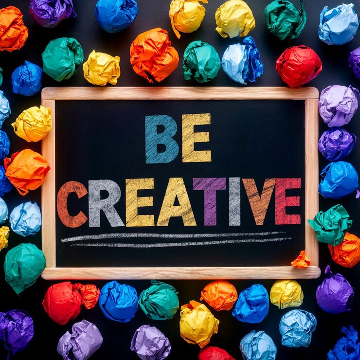 La frase Sé creativo escrita en una pizarra con coloridas bolas de papel arrugado esparcidas por todas partes