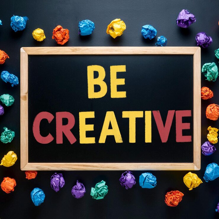 La frase Sé creativo escrita en una pizarra con coloridas bolas de papel arrugado esparcidas por todas partes