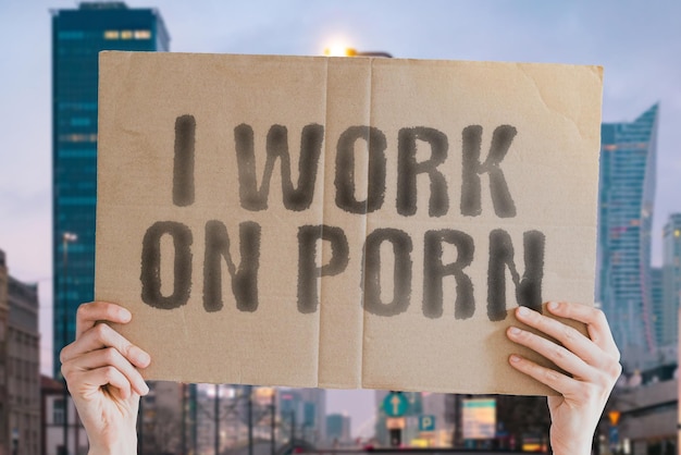 La frase "Trabajo en pornografía" en una pancarta en la mano de un hombre con fondo borroso. Seductor. Trabajo. Trabajador. Placer. Escrutinio. Anónimo. Ofensiva. Masturbación