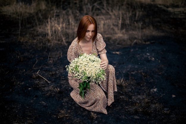 Frau 40 Jahre alt mit einem Strauß Wildblumen auf der verbrannten Erde, psychologisches Burnout-Konzept