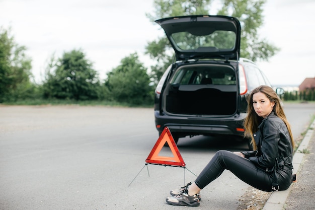 Frau alleinfahrer, der einen automotor auf reparatur- und reparaturprobleme mit unglücklich und düster überprüft