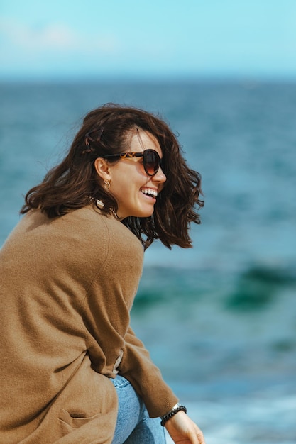 Frau am Meeresstrand, die die Kraft der Natur genießt, windiges Wetter, Sommerurlaub, Wellen im Hintergrund