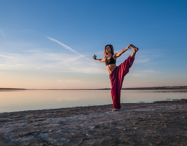 Frau am Strand bei Sonnenuntergang beginnt mit Yoga-Asana-Training. Morgendliches Aufwärmtraining mit natürlicher Dehnung