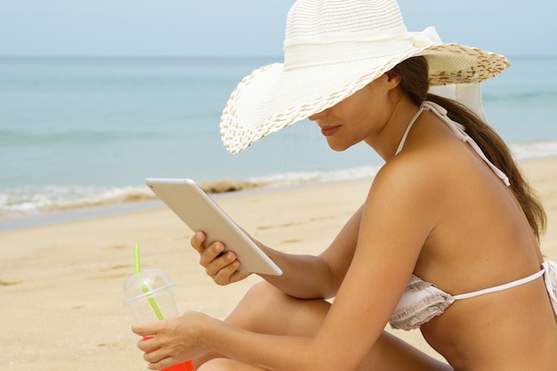 Frau am Strand mit einem Glas Cocktail und Tablette PC