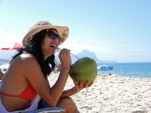 Frau am Strand trinkt Kokoswasser in Rio de Janeiro