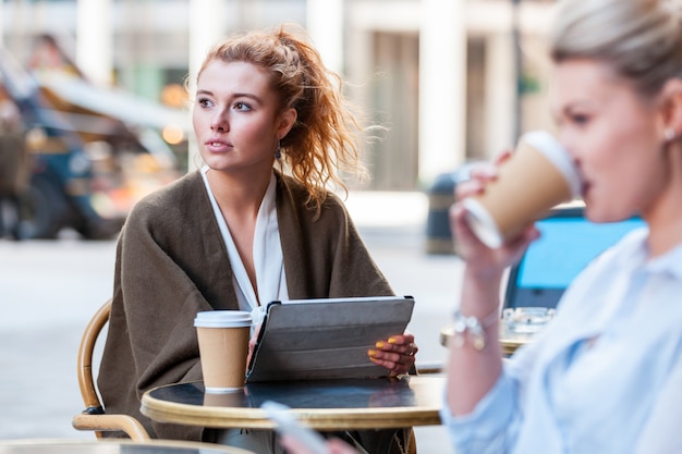 Frau an einem Café in London, das digitales Tablett hält und wegschaut