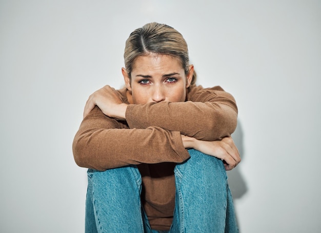 Frau Angst und Depression, während sie mit Stress Traurigkeit an einer Wand sitzt und sich unglücklich oder traurig fühlt Ernsthafte kalifornische Frau, die sich depressiv, ängstlich und besorgt fühlt, während sie einsam und verängstigt ist