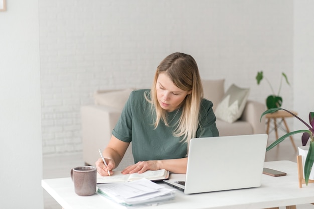 Frau arbeiten oder lernen von zu Hause mit Notizbuch, am Tisch schreibend