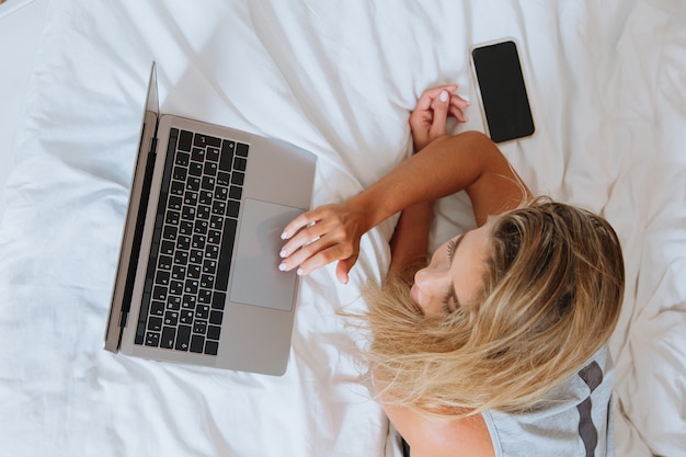 Frau arbeitet am Laptop, während sie auf dem Bett liegt