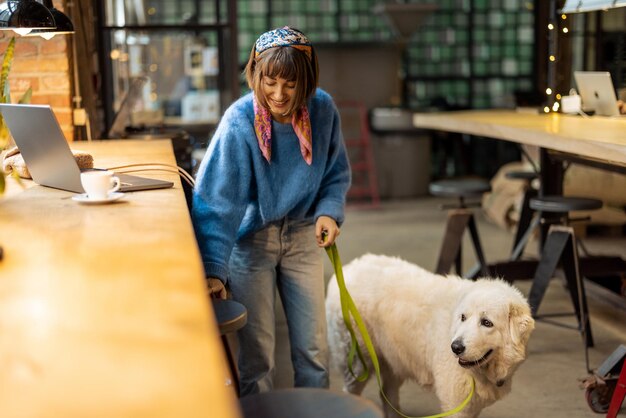 Frau arbeitet am Laptop, während sie mit ihrem Hund im modernen Café sitzt