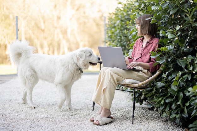 Frau arbeitet an einem Laptop, der mit Hund im Garten sitzt