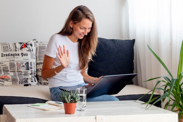 Frau arbeitet zu hause, sitze in der nähe des laptops mit notizbuch, glas wasser auf dem tisch im arbeitsbereich zu hause