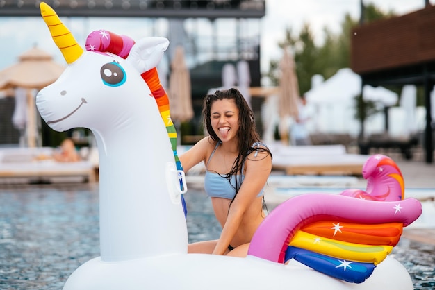 Frau auf aufblasbarer Einhorn-Spielzeugmatratze schwimmt im Pool