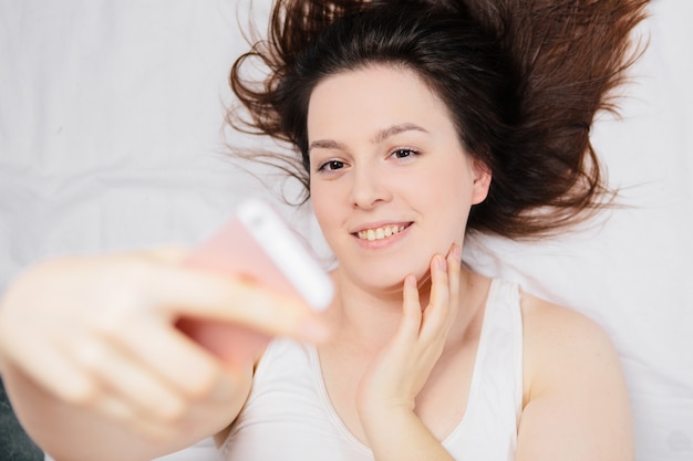 Frau auf dem Bett liegend macht Selfie am Telefon