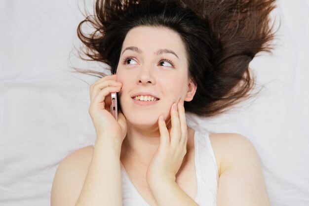 Frau auf dem Bett liegend macht Selfie am Telefon