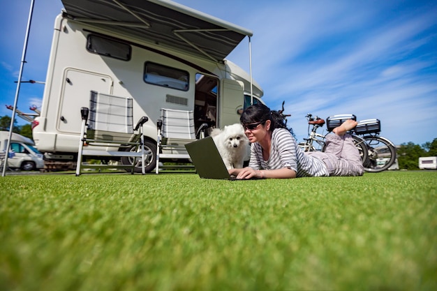 Frau auf dem Gras mit einem Hund, der einen Laptop betrachtet. Caravan Auto Urlaub. Familienurlaubsreise, Urlaubsreise im Wohnmobil