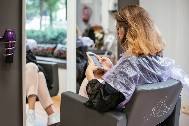 Frau auf dem Handy, das an einem Friseursalon wartet