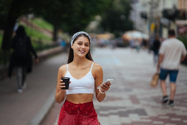 Frau auf der Straße trinkt Morgenkaffee und benutzt Smartphone