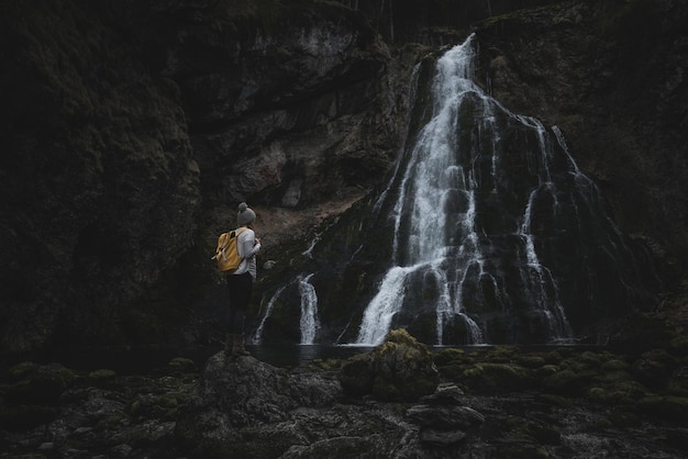 Frau auf einem Felsen, die auf einen Wasserfall schaut