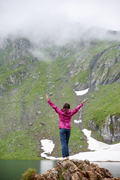 Frau auf einem Felsen mit weit geöffneten Armen und schaut auf