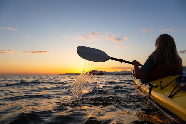 Frau auf einem Kajak paddelt während eines lebhaften Sonnenuntergangs im Ozean