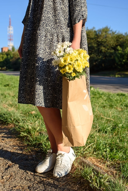 Frau auf einem spaziergang im herbsttag mit einer basteltasche mit schönen blumen. öko-tasche mit chrysanthemenblüten.