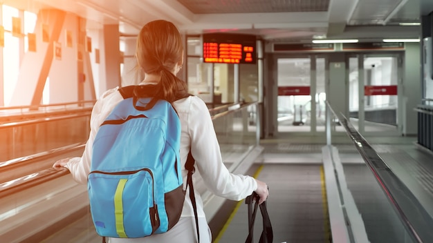 Frau auf Rolltreppe mit Rucksack und Koffer im Flughafenterminal