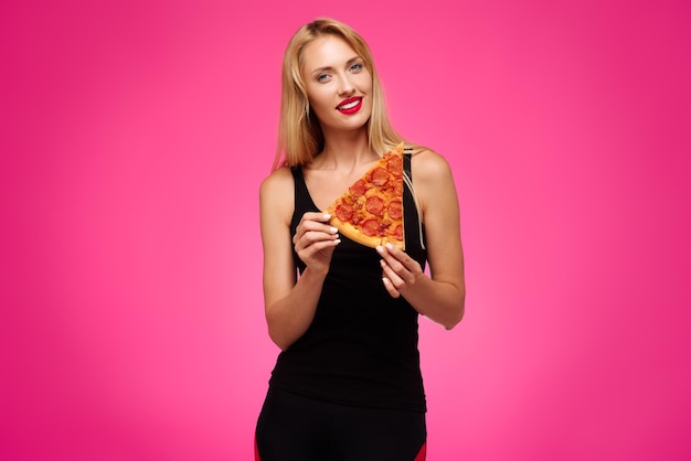 Frau auf rosafarbenem Hintergrund hält eine Pizza in ihren Händen und lächelt Konzept von gesundem und ungesundem Essen