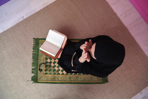 Frau aus dem Nahen Osten betet und liest den heiligen Koran, öffentliches Gut aller Muslime. Bildungskonzept der muslimischen Frau, die den heiligen Koran zu Hause oder in der Moschee im Ramadan-Monat studiert.