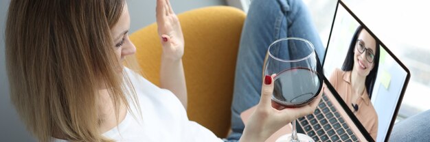 Frau begrüßt ihre Freundin per Videoanruf und hält ein Glas Wein in den Händen