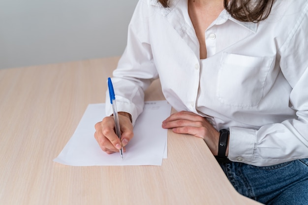 Frau bei der Arbeit. Schreiben Sie einige Papiere auf den Schreibtisch. Homeoffice oder kleine Firmensituation mit echten Menschen. Frau trägt weißes Hemd. Zugeschnittenes Foto.