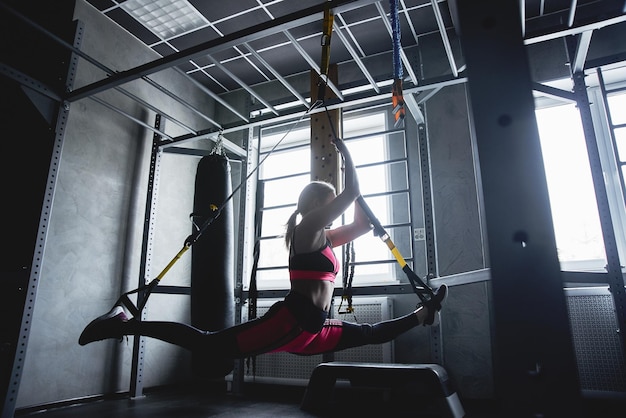 Frau beim Fitnesstraining im Fitnessstudio Dehnübungen an TRX-Bändern