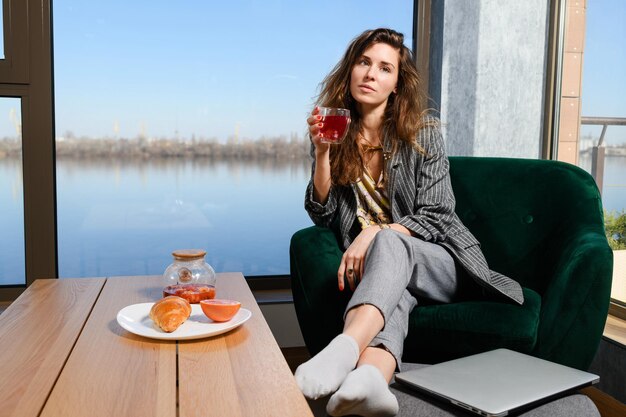 Frau beim Frühstück mit Tee und Laptop