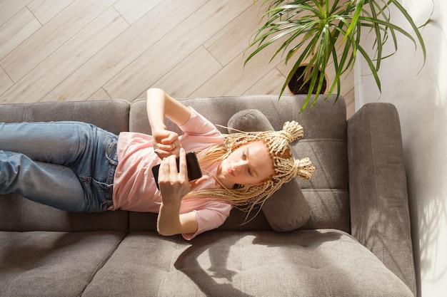 Frau benutzen ein Smartphone, während sie auf einem Sofa liegen. Draufsicht. Online studieren, freiberuflich tätig.