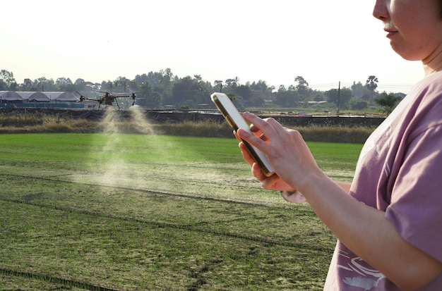 Frau benutzt ein Handy auf einem Bauernhof, umgeben von Landwirtschaftskontrollen Petrol Drone Sprayer