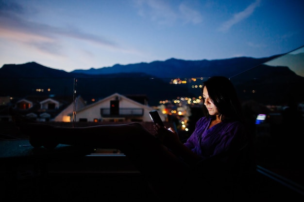 Foto frau benutzt ein smartphone, während sie auf dem balkon sitzt