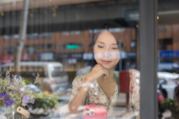 Frau benutzt Handy und sitzt in einem Café mit Fensterreflexion